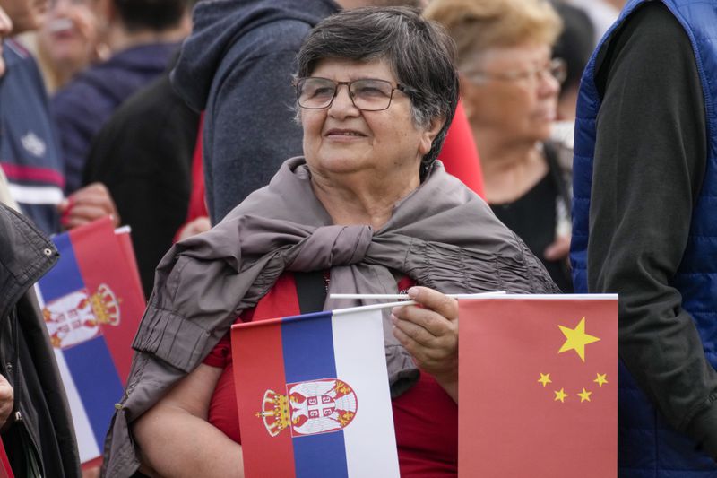 A woman holds the Chinese and Serbian flags as she waits for the arrival of Chinese President Xi Jinping with his Serbian counterpart Aleksandar Vucic at the Serbia Palace in Belgrade, Serbia, Wednesday, May 8, 2024. (AP Photo/Darko Bandic)