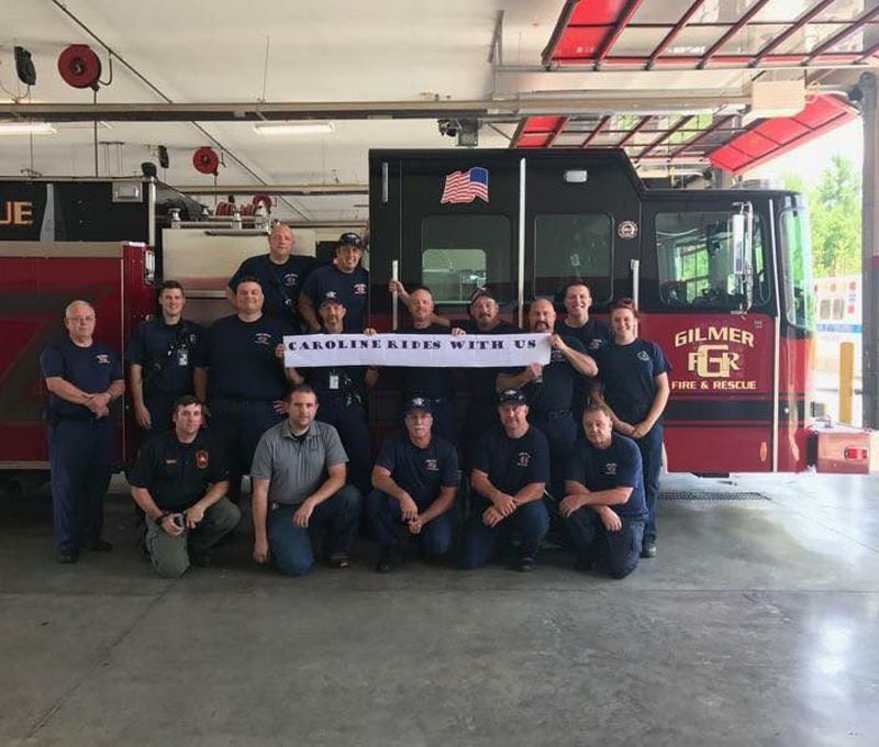 Firefighters in Gilmer County hold a sign that reads “Caroline rides with us,” as a show of support for their fellow firefighter, Gary Wirl, whose daughter Caroline was injured July 4 and has been in intensive care since then. Photo: courtesy Wirl family.