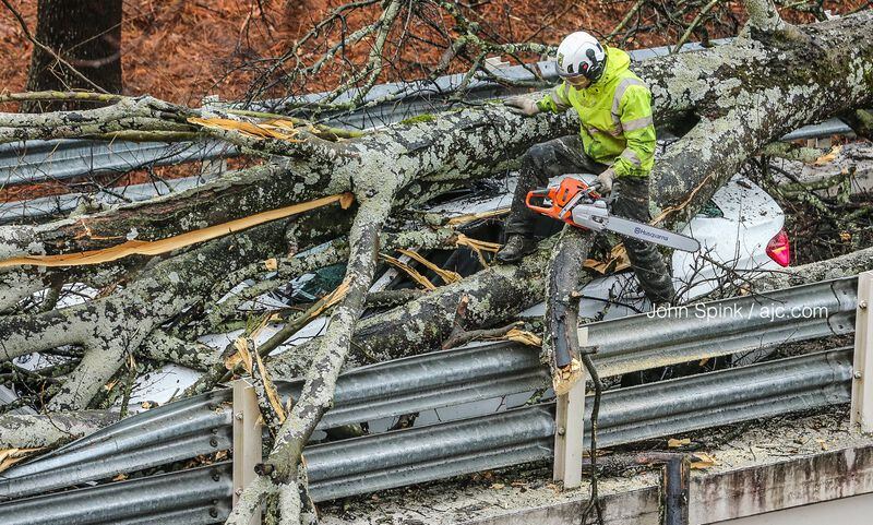A worker uses a chainsaw to cut through the branches of a downed tree that fell across the entrance ramp to an Emory University Hospital parking deck. JOHN SPINK / JSPINK@AJC.COM