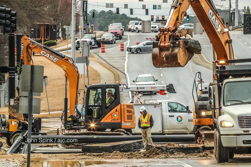 Workers with Gwinnett County Department of Transportation  repaired a water main break on Indian Trail Road before filling a massive hole caused when part of the road collapsed. JOHN SPINK / JSPINK@AJC.COM