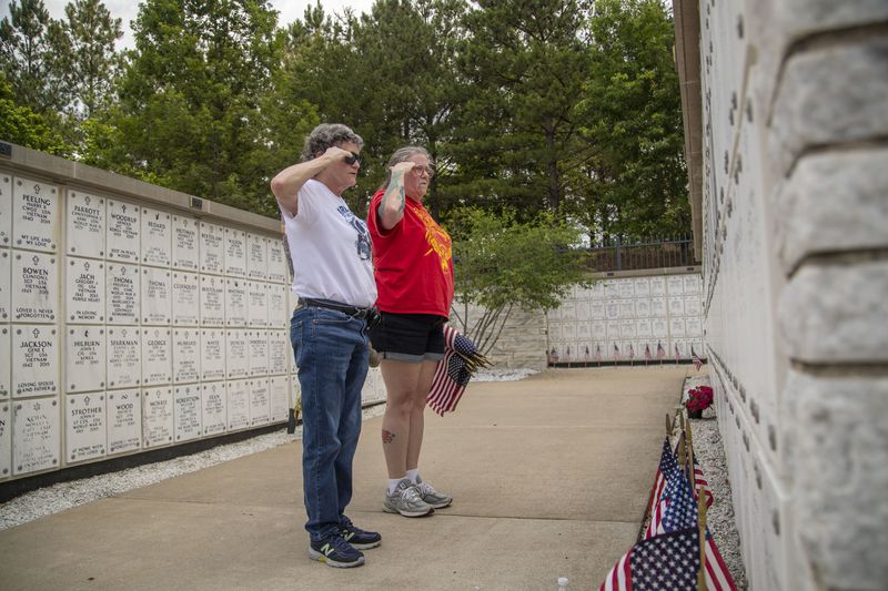 Ann Poche, right, and Jaye McKinney-Rheal, left, salute the headstones where they placed an American flag at the Georgia National Cemetery in Canton on Memorial Day in 2021.  (AJC FILE)