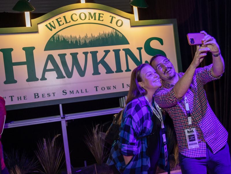 The "Stranger Things: The Experience" at Pullman Yards begins where Whitney and Adam Kemmerick of Kirkwood take pics with the Welcome to Hawkins sign on Friday, Nov. 11, 2022.  (Jenni Girtman for The Atlanta Journal-Constitution)