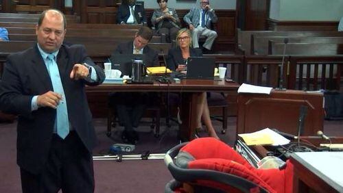 Defense attorney Bryan Lumpkin cross-examines a police witness on Wednesday. The car seat in which Cooper Harris died is visible at right. (Screen capture from WSB-TV video)