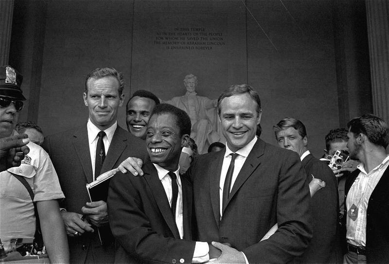 Aktorius Marlonas Brando (dešinėje) pozuoja apsikabinęs Jamesą Baldwiną, autorių ir pilietinių teisių lyderį, priešais Linkolno statulą Linkolno memoriale 1963 m. rugpjūčio 28 d. per žygio Vašingtone demonstravimo ceremonijas po masinio parado.  Kartu su jais pozuoja aktoriai Charltonas Hestonas (kairėje) ir Harry Belafonte.  AP NUOTRAUKA