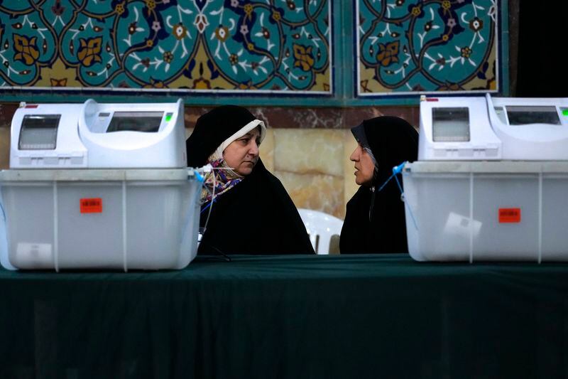 Staff members of a polling station talk during the parliamentary runoff elections in Tehran, Iran, Friday, May 10, 2024. Iranians voted Friday in a runoff election for the remaining seats in the country's parliament after hard-line politicians dominated March balloting. (AP Photo/Vahid Salemi)