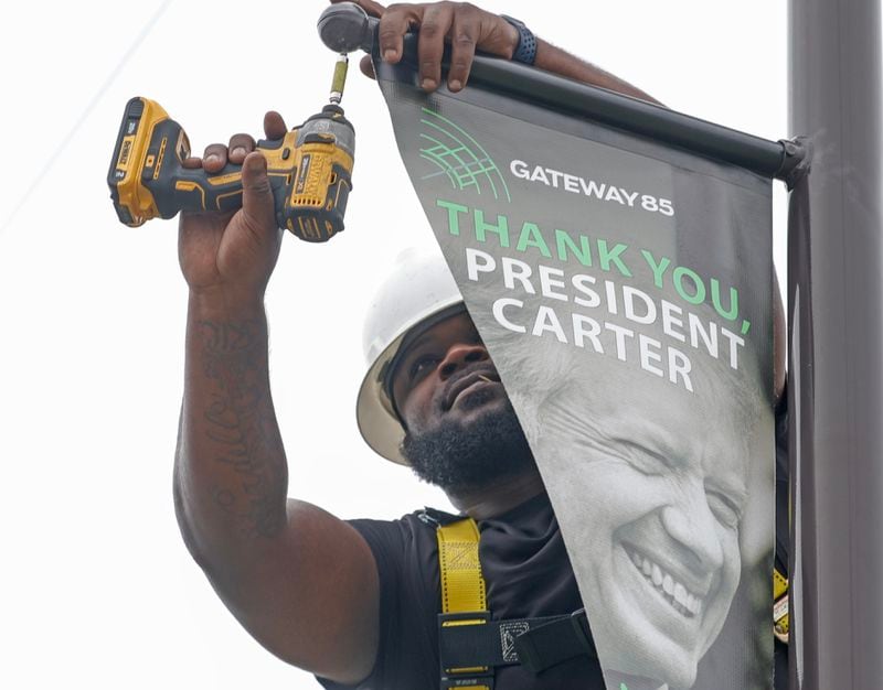 Kyle Williams, a sign installer for Alpha Graphics puts up a banner on Jimmy Carter Boulevard in Norcross on Monday, May 22, 2023. (Natrice Miller/The Atlanta Journal-Constitution)