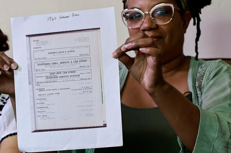 Yolanda Mullins, granddaughter of Charlie Hunter Sr. holds up a copy of a listing of his store in the Negro Motorist Green Book on Friday, July 29, 2022. (Natrice Miller/natrice.miller@ajc.com)