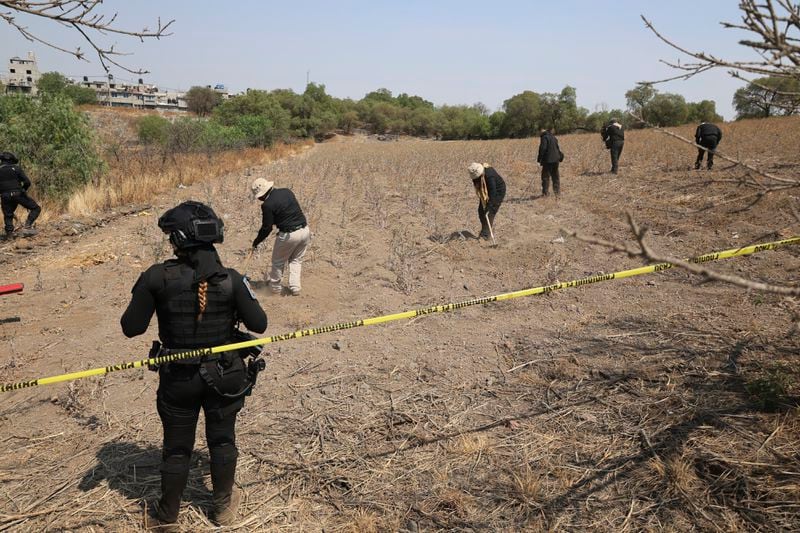 Police stand by as members of the National Search Commission use rakes to search an area where volunteers said they found a clandestine crematorium in Tlahuac, on the edge of Mexico City, Wednesday, May 1, 2024. Ceci Flores, a leader of one of the groups of so-called "searching mothers" from northern Mexico, announced late Tuesday that her team had found bones around clandestine burial pits and ID cards, and prosecutors said they were investigating to determine the nature of the remains found. (AP Photo/Ginnette Riquelme)