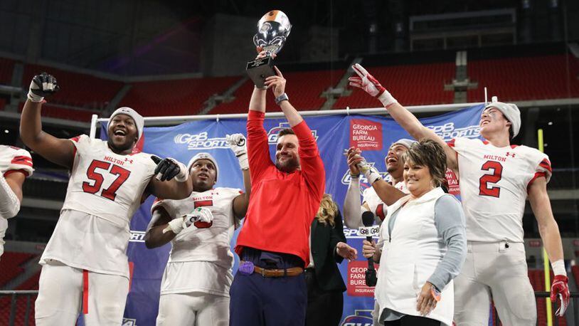 Milton coach Adam Clack celebrates with the trophy with players from left; Paul Tchio (57), Jordan Davis, Jordan Yates, and Dylan Leonard after their 14-13 win against Colquitt County in the Class AAAAAAA State Championship at Mercedes-Benz Stadium Wednesday, December 12, 2018, in Atlanta. Milton won 14-13. (JASON GETZ/SPECIAL TO THE AJC)
