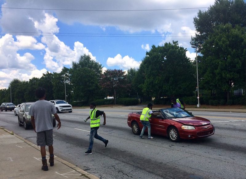 Marc KD Boyd gives instructions to water sellers at the corner of Northside Drive and Joseph E. Boone Blvd as Sheldon Peoples, 16, hustles to the safety of the sidewalk. Photo by Bill Torpy