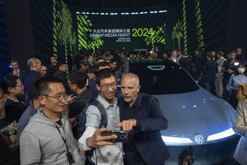 Attendees pose for photos near the latest cars unveiled during a media event held by the Volkswagen Group a day before the auto show in Beijing, Wednesday, April 24, 2024. The Volkswagen Group, which includes Audi and Porsche, plans to launch 40 new models in China over the next three years and to have a lineup of 30 EVs by 2030. (AP Photo/Ng Han Guan)