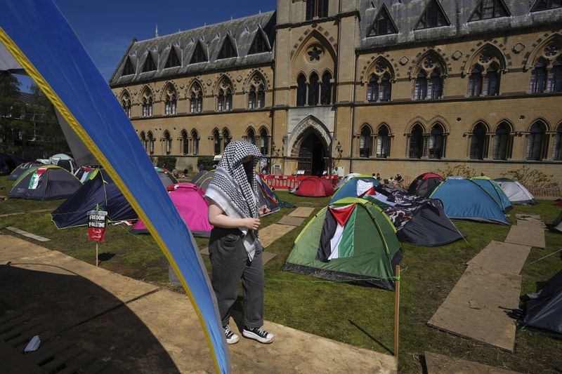 A pro-Palestinian walks past tents outside the Pitt Rivers Museum at Oxford in England, Thursday, May 9, 2024. Students in the UK, including in Leeds, Newcastle and Bristol, have set up tents outside university buildings, replicating the nationwide campus demonstrations which began in the US last month. (AP Photo/Kin Cheung)