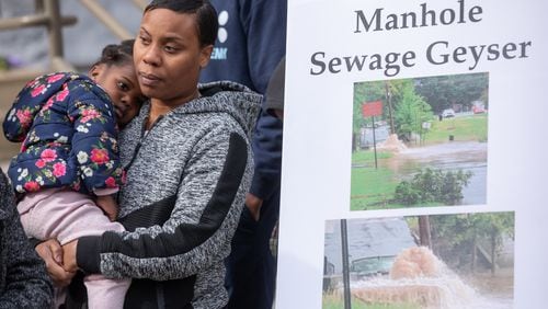 Westside families stand next to photos of sewage spills and flooded homes during a press conference to announce a lawsuit against the city of Atlanta over flooding issues on Feb. 29, 2024.