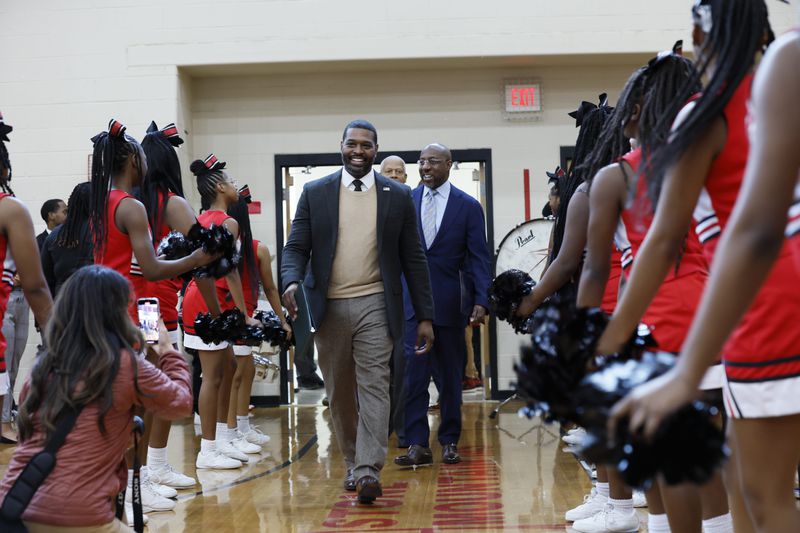 U.S. Environmental Protection Agency Administrator Michael S. Regan, flanked by U.S. Sen. Raphael Warnock, D-Ga., is greeted by cheerleaders as they walk into the Stone Mountain Middle School gym on Monday, Jan. 8, 2024. The DeKalb County School District received a $20 million grant from the EPA to purchase electric school buses. (Miguel Martinez /miguel.martinezjimenez@ajc.com)