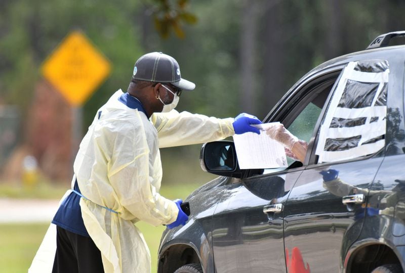 A medical worker in protective gear helps a potential COVID-19 patient with paperwork at a Phoebe Putney Health System drive-through testing site in Albany on Tuesday, March 24, 2020. HYOSUB SHIN / HYOSUB.SHIN@AJC.COM