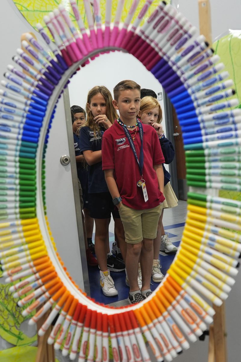 Students are reflected in a mirror as they wait to enter teacher Lindsey Wuest's Science As Art classroom, at A.D. Henderson School in Boca Raton, Fla., Tuesday, April 16, 2024. When teachers at the K-8 public school, one of the top-performing schools in Florida, are asked how they succeed, one answer is universal: They have autonomy. (AP Photo/Rebecca Blackwell)