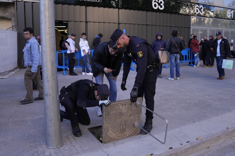 Police officers check and seal the sewage system adjacent to the Santiago Bernabeu stadium, before the Champions League quarterfinal first leg soccer match between Real Madrid and Manchester City in Madrid, Spain, Tuesday, April 9, 2024. This week's Champions League soccer games will go ahead as scheduled despite an Islamic State terror threat. A media outlet linked to the terror group has issued multiple posts calling for attacks at the stadiums hosting quarterfinal matches in Paris, Madrid and London. (AP Photo/Manu Fernandez)