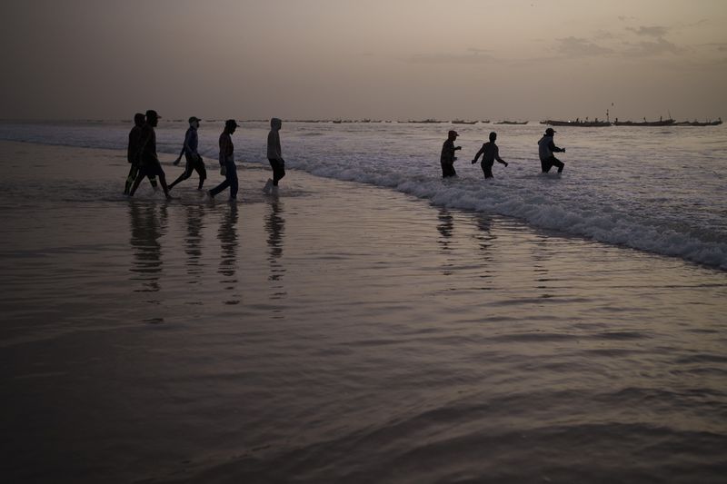 This image provided by World Press Photo is part of a multimedia project by Associated Press' Renata Brito and Felipe Dana titled Adrift, won the World Press Photo Africa Regional Winner Open Format category and shows young fishermen walk into the ocean to board an artisanal fishing boat in Nouakchott, Mauritania, Friday, Dec. 10, 2021. In May 2021 a boat from Mauritania full of dead men was found off the coast of the Caribbean Island of Tobago. Who were these men and why were they on the other side of the Atlantic Ocean? Two visual journalists sought answers, uncovering a story about migrants from West Africa who seek opportunity in Europe via an increasingly popular but treacherous Atlantic route. (AP Photo/Felipe Dana)