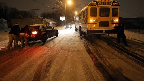 People work to push a stuck Atlanta school bus and a car on an icy stretch of University Avenue in Southwest Atlanta on Tuesday evening January 28, 2014. The bus was eventually moved off the road and left for the night.
