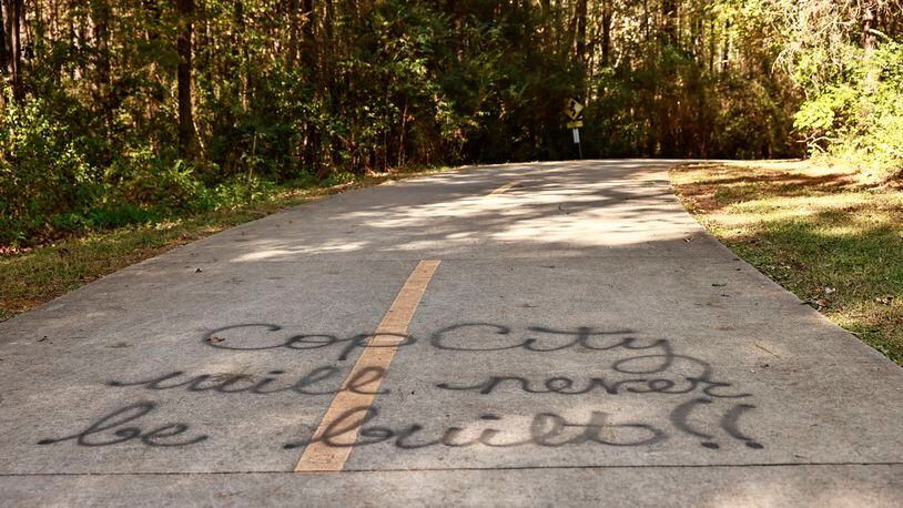 Text that reads "Cop City Will Never Be Built" is written on a sidewalk near forested land that is the proposed site of Atlanta's new police and fire training facility, as seen on Friday, October 21, 2022. (Natrice Miller/natrice.miller@ajc.com)