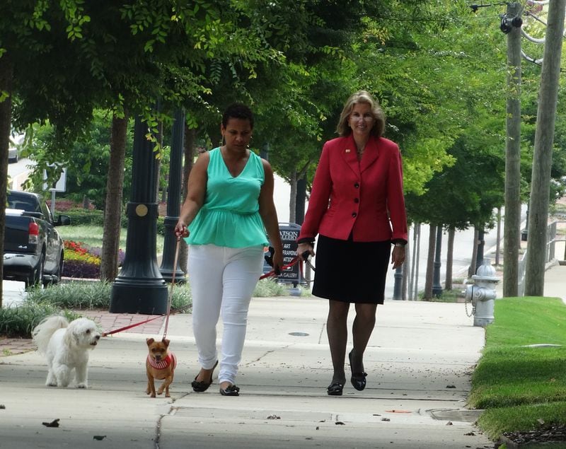 Teya Ryan and another dog owner walk their pets while the protesters watch. CREDIT: Rodney Ho/rho@ajc.com