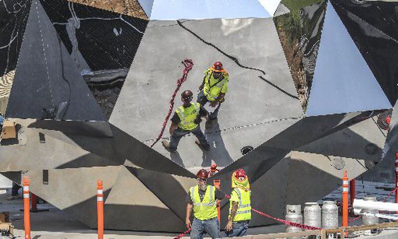 Workers are reflected in the 35-foot mirrored soccer ball sculpture on the north plaza of Mercedes-Benz Stadium on Thursday, where construction continues on the 11-acre greenspace that will be used for tailgating and parking on game days. JOHN SPINK / JSPINK@AJC.COM