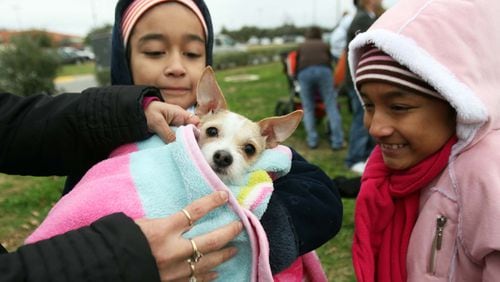 Sisters Marisol and Isabel Vasquez bundle their dog Pebbles in a blanket during a wintertime vaccination drive in 2009.