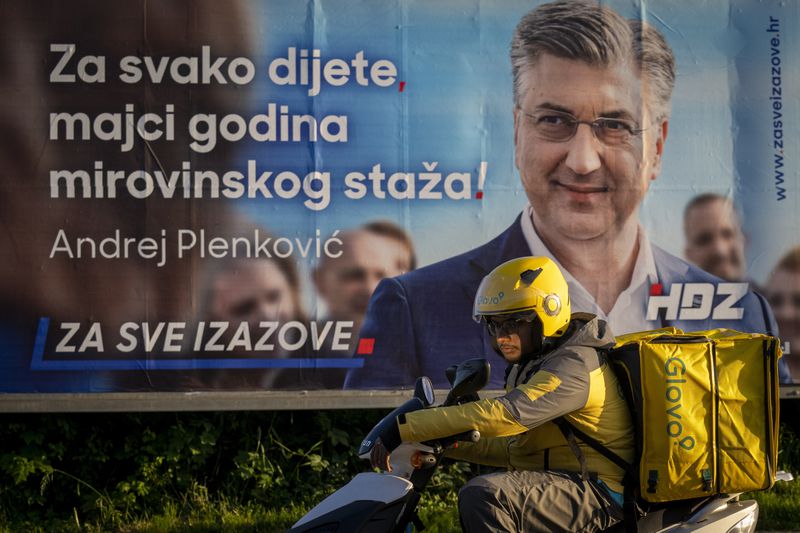 A delivery man waits for green light on a street in front of an election poster in Zagreb, Croatia, Sunday, April 14, 2024. Croatia this week holds an early parliamentary election following a campaign that was marked by heated exchanges between the country's two top officials, creating a political crisis in the Balkan country, a European Union and NATO member state. (AP Photo/Darko Bandic)