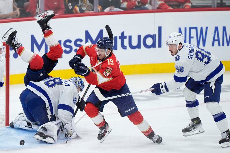 Florida Panthers defenseman Brandon Montour flips over Tampa Bay Lightning goaltender Andrei Vasilevskiy (88) as left wing Matthew Tkachuk (19) chases the puck followed by defenseman Mikhail Sergachev (98) during the first period of Game 5 of the first-round of an NHL Stanley Cup Playoff series, Monday, April 29, 2024, in Sunrise, Fla. (AP Photo/Wilfredo Lee)