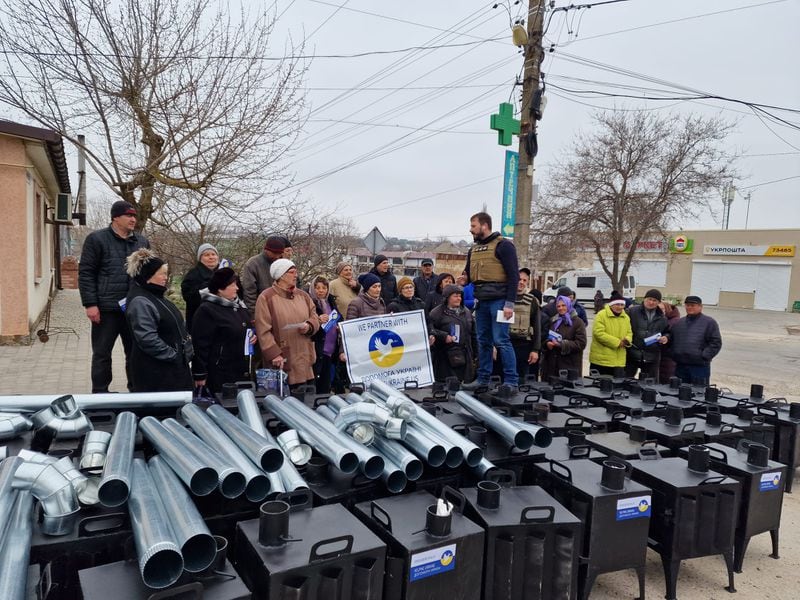 A member of a church in Odessa, Ukraine organizes volunteers to prepare to install wood-burning stoves. The banner reads "Partnering with HelpingUkraine.US. Courtesy HelpingUkraine.US.