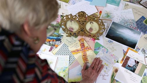 Clarissa Strickland, whose sister Nan Durrett, 74, died last month after developing a fever and cough at an assisted living facility, looks over the many dozens of sympathy cards she has placed around framed photographs of herself (left) and her sister (right) at her home in Lilburn. The family believes Durrett didn’t receive adequate care at the facility. When she was hospitalized, a physician told the family Durrett had COVID-19. (Curtis Compton / ccompton@ajc.com)