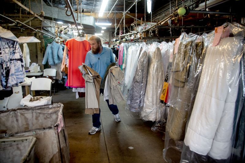 Sig Samuels Dry Cleaners co-owner Steve Collins delivers clothes for pressing while walking past lines of cleaned comforters earlier this month. Some customers have been bringing in more items like comforters to help Collins tide over the loss of business from clothes. STEVE SCHAEFER FOR THE ATLANTA JOURNAL-CONSTITUTION