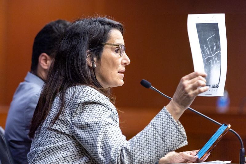 Parent Beth Gann, speaking in March in favor of legislation that would make antisemitism a hate crime legislation, holds a photo of a swastika that was painted on a wall as an act of vandalism. (Arvin Temkar / arvin.temkar@ajc.com)