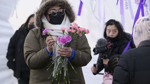 Liliana Luna hands out flowers to attendees of a ceremony honoring the victims of last year's spa shootings held Saturday, March 12, 2022, at Blackburn Park in Atlanta. (Photo: Daniel Varnado for the Atlanta Journal-Constitution)