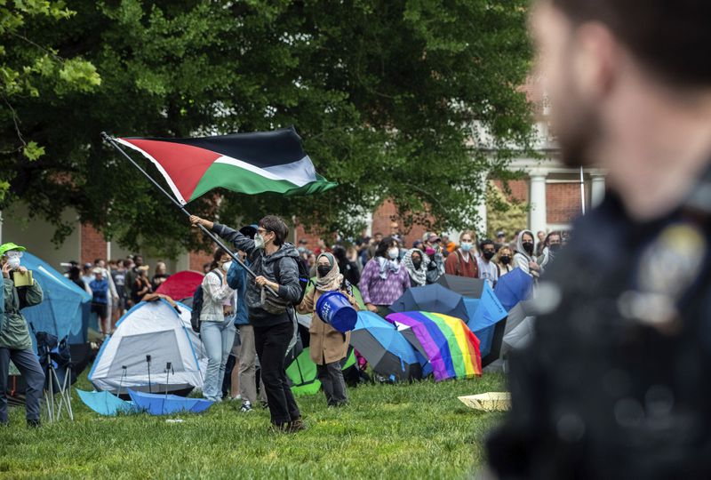 A police officer, right, watches a protester wave a Palestinian flag on the grounds of the University of Virginia, in Charlottesville, Va., where tents are set up, Saturday, May 4, 2024. (Cal Cary/The Daily Progress via AP)