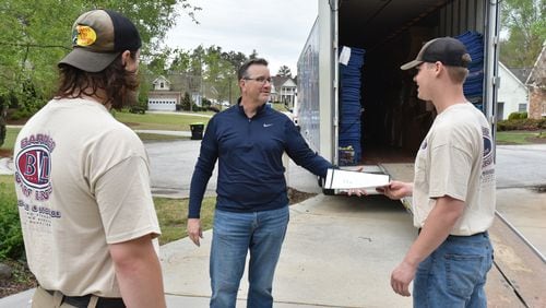 Chris New (center), owner of Barnes Van Lines, hands over paperwork to Anson Strickland as Joe Nowak (left) looks on while moving a family in Villa Rica on Thursday, April 15, 2021. (Hyosub Shin / Hyosub.Shin@ajc.com)