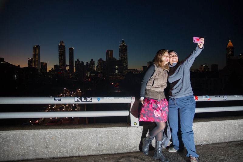 Two women take a selfie in front of the Atlanta skyline on the Jackson Street Bridge at sunset. On a clear night, the bridge can attact dozens of photographers to catch the sunset. (SPECIAL/BRANDEN CAMP)