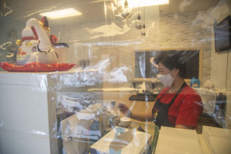 Jane Chung, owner of Family Baking, stands behind two clear shower curtains as she rings up a customer at her store inside the Atlanta Chinatown Shopping Mall in Chamblee, Friday, July 31, 2020. The clear curtains are used as a barrier to protect both employees and customers from transmitting germs while in the store. (ALYSSA POINTER / ALYSSA.POINTER@AJC.COM)