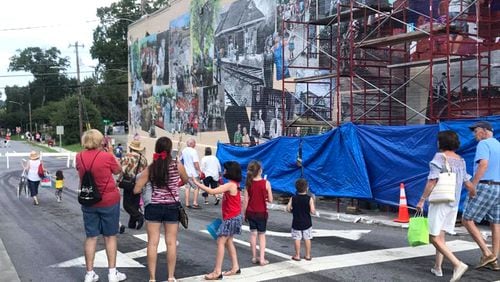 Passersby watch the work in progress of the Woodstock Community Mural. A ribbon-cutting to unveil the completed mural is set for 6 p.m. Saturday, July 21, in downtown Woodstock. WOODSTOCK COMMUNITY MURAL via Facebook
