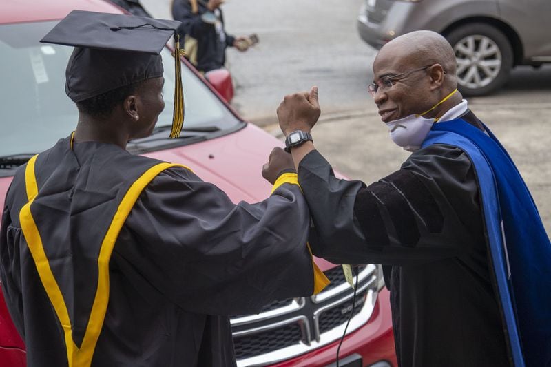 Frederick Douglass High School principal Ellis Duncan (right) congratulates a graduating senior with an elbow bump during a drive-thru celebration event at the school in Atlanta's Center Hill community, Wednesday, May 20, 2020. Graduating seniors were given their diplomas, cap, gowns and academic and athletic awards during the drive-thru event at the school. Students were also given a chance to be photographed win their cap and gown which was provided by the Frederick Douglass High School Alumni Association. (ALYSSA POINTER / ALYSSA.POINTER@AJC.COM)