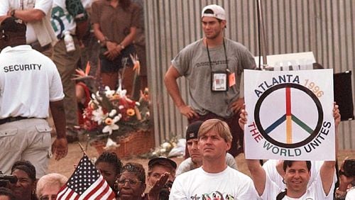 With a bouquet of flowers (background) marking the point of detonation of Saturday's fatal bombing, Olympic fans gather for a memorial ceremony at the reopening of Centennial Park at the Centennial Summer Olympics in Atlanta on Tuesday, July 30, 1996. (AP Photo/John Gaps III)