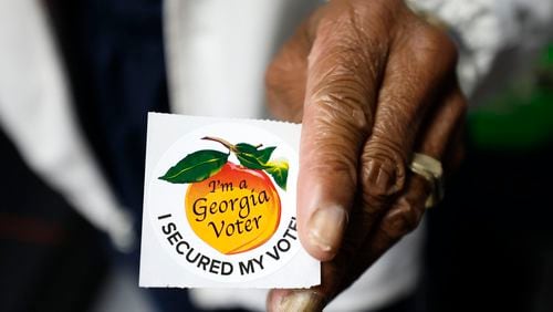 A poll worker holds a Georgia voter sticker ready to be handed to a voter on Oct. 17, 2022. (Miguel Martinez/The Atlanta Journal-Constitution
