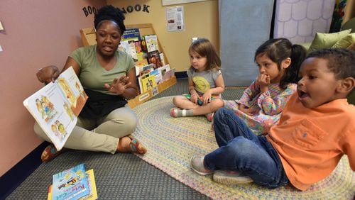 Ashton Aiken reads a book to (from left) Liliana Woods, 4, Carmen Castro, 3 and Eric Revell, 3, at Sheltering Arms International Village Center in 2018. HYOSUB SHIN / HSHIN@AJC.COM