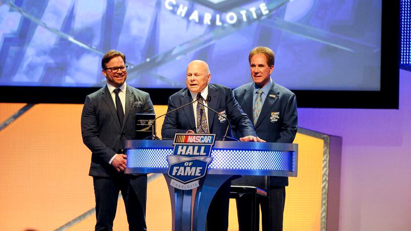 Hall of Fame inductee Bruton Smith, center entertains the crowd as his son, Marcus Smith, left and Hall of Fame member Darrell Waltrip, right look on during the NASCAR Hall of Fame Induction ceremony in Charlotte, N.C., Saturday, Jan. 23, 2016. (AP Photo/Mike McCarn)