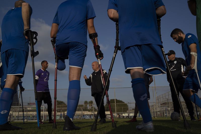 The coach of the Israel Amputee Football Team, Sharon Paz, center, gives instructions to his players during a practice session in Ramat Gan, Thursday, April 11, 2024. The team practices twice a week in the evening at a stadium in Ramat Gan. Altshuler Shaham Investment House is a financial sponsor of the team, but more sponsors are being sought to help defray the costs of competition and travel. (AP Photo/Leo Correa)