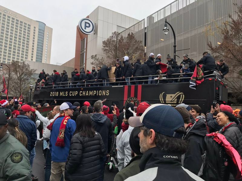 Atlanta United team members ride on an open-top bus, carrying the MLS Cup trophy with them