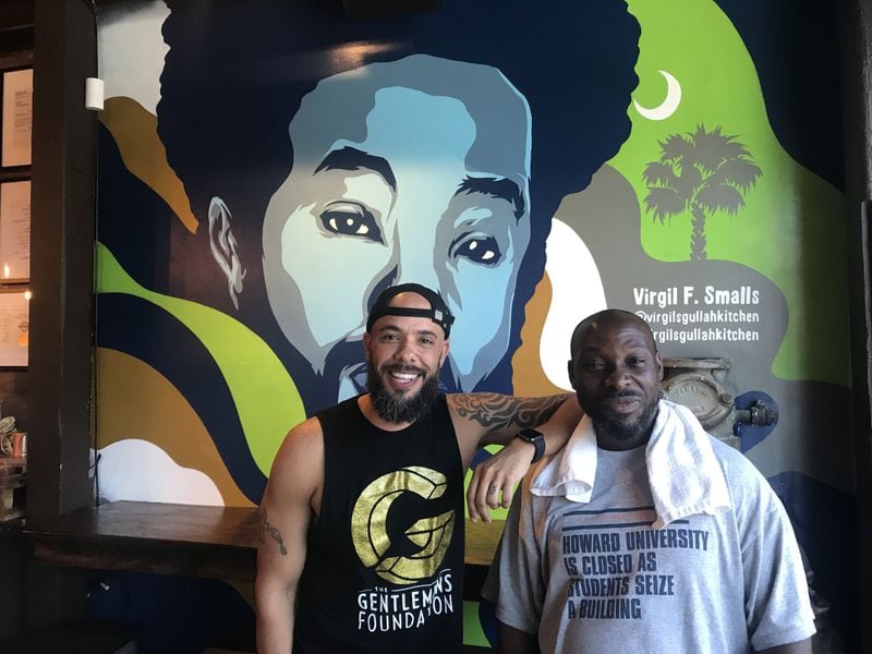 Virgil’s Gullah Kitchen and Bar’s co-owner, Gee Smalls, and artist C. Flux Sing stand in front of the mural that Sing painted of Smalls’ father, Virgil F. Smalls, the restaurant’s namesake. LIGAYA FIGUERAS / LFIGUERAS@AJC.COM.