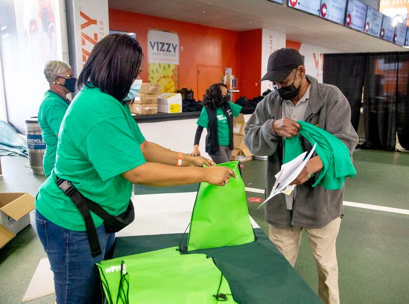 Fulton County Schools employee Lashanda Brown (left) hands out gift bags to people after receiving their vaccination shot at the Mercedes-Benz Stadium on Monday.  STEVE SCHAEFER FOR THE ATLANTA JOURNAL-CONSTITUTION