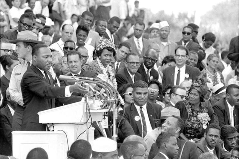 According to legend, midway through Martin Luther King Jr.'s March on Washington address, gospel great Mahalia Jackson, shouted at him to "Tell ‘em about the dream." King immediately shifted the tone of his speech to what we know today as the "I Have a Dream," speech. In this photo, Jackson is seated below King to his right wearing a flower on her dress. She is looking at him. 