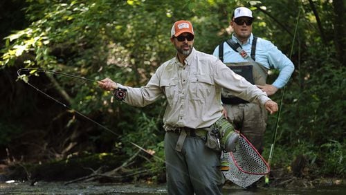 Atlanta resident Louis Cahill (left), 55, hooks a trophy-size trout while Justin Pickett, 33, of Newnan, spots them on a catch and release stream at Noontootla Creek Farms. Curtis Compton/ccompton@ajc.com